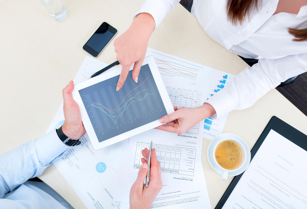 Hands pointing at tablet showing data graphs